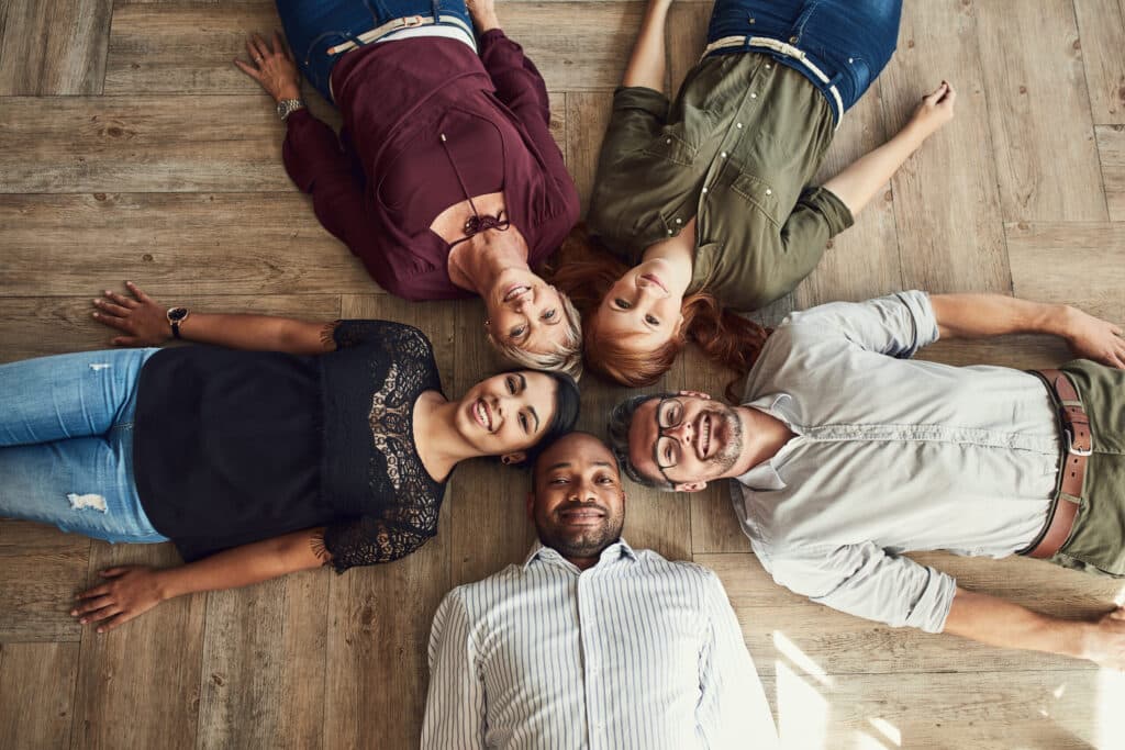 High angle portrait of a group of colleagues lying together in a circle on the floor at work.